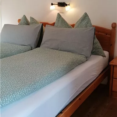 Ein gemütliches Schlafzimmer mit einem Holzbett und Kissen in sanften Farben. An der Wand hängt ein Bild von einem Highland-Rind.