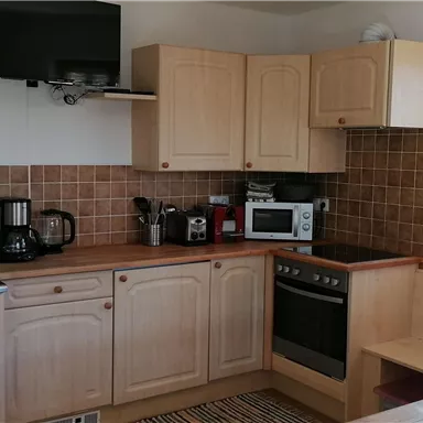 Eine moderne Küche mit Holzschränken und einem Fenster, das natürliches Licht hereinlässt. Sie ist ausgestattet mit einem Herd, einer Mikrowelle und weiteren Küchengeräten.