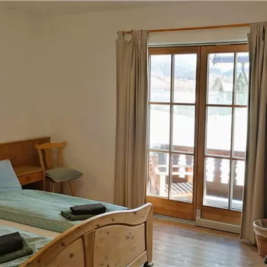 Ein helles Zimmer mit zwei Betten, Holzmöbeln und einem Fenster mit Blick auf die Natur. Der Raum ist einfach und gemütlich eingerichtet.