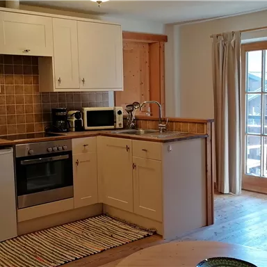 Eine moderne Küchenzeile mit weißen Schränken und einem Esstisch. Große Fenster sorgen für viel Tageslicht in einem gemütlichen Raum.