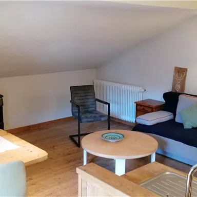 Ein gemütlicher Wohnraum mit einer bequemen Couch und einem Holzstuhl. Ein Tisch und ein Regal runden die einladende Atmosphäre ab.