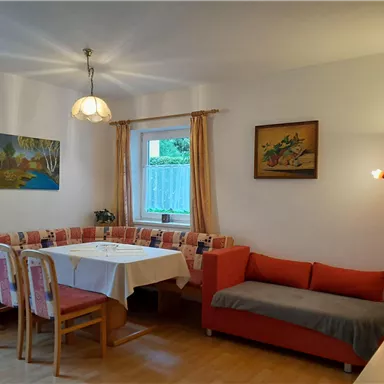 A cozy living space with a dining area and a red sofa. Bright walls and artwork give the room an inviting atmosphere.