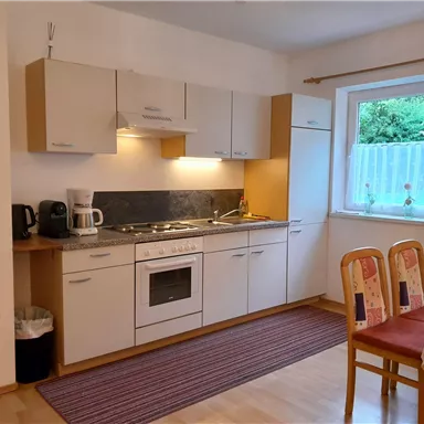 A modern kitchen with white cabinets and a stove. There is a table with chairs and a window that lets in daylight.