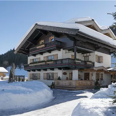 Ein charmantes Chalet im Winter mit schneebedecktem Grundstück. Die sonnigen Fenster und Balkone verleihen dem Gebäude einen einladenden Charakter.