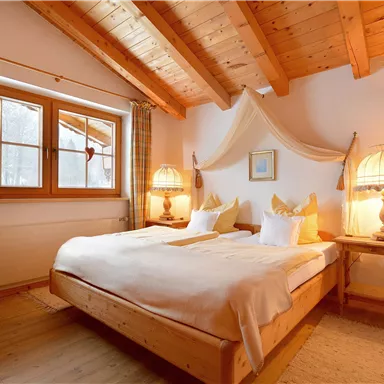 A cozy bedroom with a wooden ceiling and two beds. There are large windows and warm light from the table lamps.