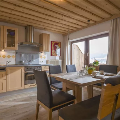 A modern kitchen with wooden shelves and a dining table. Plenty of light streams through the window, creating a cozy atmosphere.