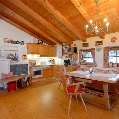 A cozy kitchen with a wooden ceiling and a rustic dining table. The walls are adorned with decorations and windows that let in plenty of light.