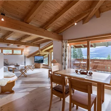 A cozy living space with a wooden ceiling and large windows. The room offers a view of the mountains and has an inviting dining area.
