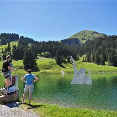 A beautiful lake surrounded by green hills and trees. People enjoy nature and the sun by the shore.