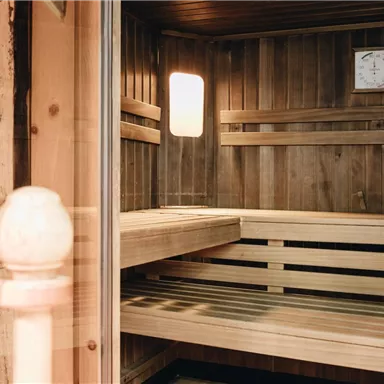 Eine moderne Sauna aus Holz mit Bänken und einer Uhr an der Wand. Das Licht fällt sanft durch das Fenster und schafft eine entspannende Atmosphäre.