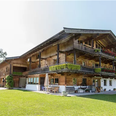 A charming wooden house with several balconies and green plants. The surrounding lawn and trees create an inviting atmosphere.