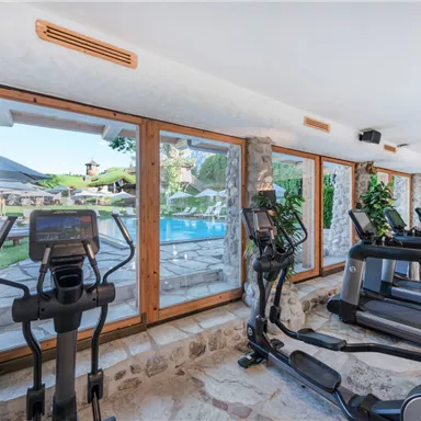 A modern gym overlooking a pool. Large windows let in plenty of light, and there are some green plants visible.