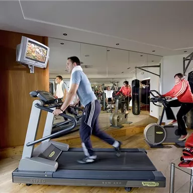 A modern gym with several training machines. Two people are working out on the treadmill and the cross trainer.