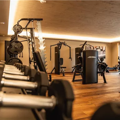 Ein modernes Fitnessstudio mit verschiedenen Trainingsgeräten und einer angenehmen Holzfußboden. Die Beleuchtung sorgt für eine einladende Atmosphäre.