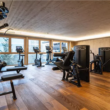 Ein modernes Fitnessstudio mit verschiedenen Sportgeräten und großen Fenstern. Der Boden ist aus Holz und sorgt für eine einladende Atmosphäre.