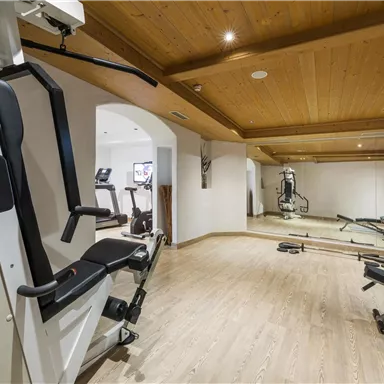 A modern gym with various training equipment. The room has a warm wooden look and ample space for fitness activities.