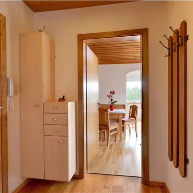 A bright hallway with wooden flooring and a wardrobe. In the background, a dining area can be seen.