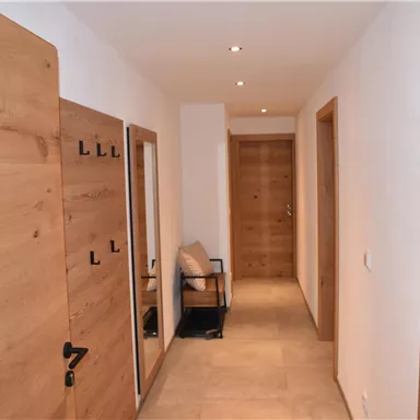 Ein heller Flur mit Holzrollen und modernen Wänden. Auf der linken Seite befindet sich ein Stuhl und mehrere Türen.