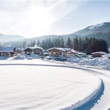 A snowy landscape with houses and mountains in the background. The sun shines over the winter landscape.