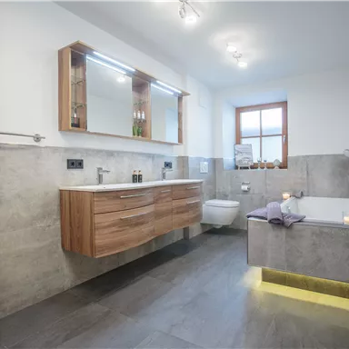 Ein modernes Badezimmer mit Holzwaschtisch und eleganter Badewanne. Die sanfte Beleuchtung schafft eine entspannende Atmosphäre.