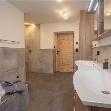 Ein elegantes Badezimmer mit einer Badewanne und einem modernen Waschbecken. Es ist stilvoll und gut beleuchtet, mit warmen Holzelementen und sanftem Licht von Kerzen.