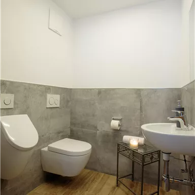 Ein modernes Badezimmer mit einer Toilette und einem Waschbecken. Die Wände sind teilweise grau, und ein Holzboden verleiht Wärme.