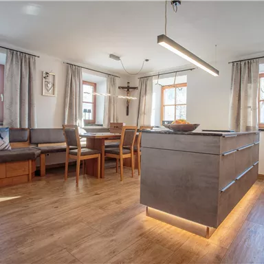 Eine moderne Küche mit Holzfußboden und großen Fenstern. Das gemütliche Esszimmer ist mit einem Tisch und Stühlen sowie einer Sitzbank ausgestattet.