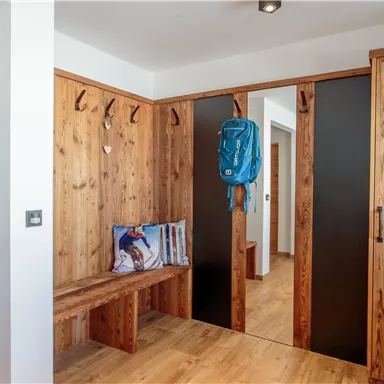 Ein einladender Eingangsbereich aus Holz mit einer Bank und Garderobenhaken. Im Hintergrund sind Türen zu weiteren Räumen sichtbar.