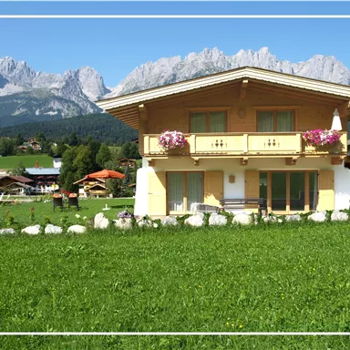 Ein schönes, traditionelles Haus in einer malerischen Landschaft. Die Berge im Hintergrund und der grüne Rasen schaffen eine idyllische Atmosphäre.