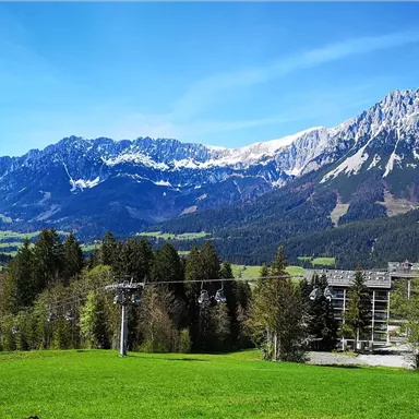 Eine malerische Landschaft mit beeindruckenden Bergen und schneebedeckten Gipfeln. Im Vordergrund befindet sich eine grüne Wiese, die eine ruhige Atmosphäre schafft.