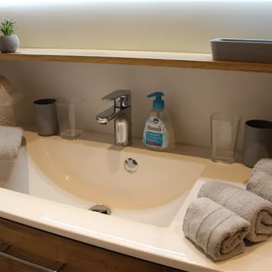 Ein modernes Badezimmer mit einem Waschbecken und Handtüchern. Auf dem Waschbecken stehen Seife und Gläser.