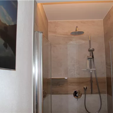 Eine moderne Duschkabine mit transparenten Wänden und einer schlichten Dusche. Im Hintergrund ist ein Bild mit einem Sonnenuntergang zu sehen.