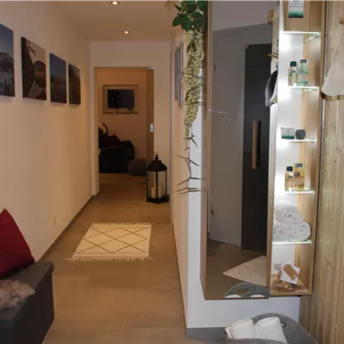 Ein heller Flur mit modernen Dekorationen und einem großen Spiegel. Auf der linken Seite sind Bilder an der Wand und ein gemütlicher Sitzbereich.