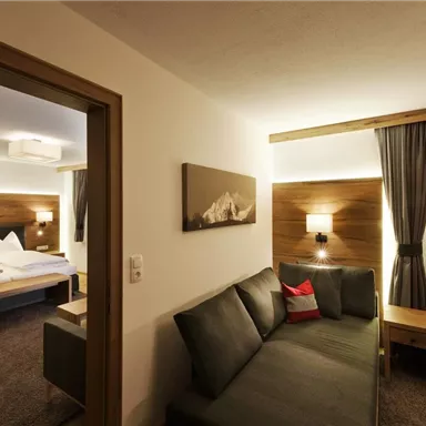 A cozy room with a sofa and a double bed. The warm wood details and soft lighting create an inviting atmosphere.