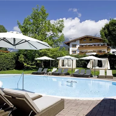 A beautiful swimming pool with loungers and parasols in a well-kept garden. In the background, trees and a holiday home are visible.