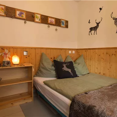 Ein gemütliches Schlafzimmer mit Holzvertäfelung und dekorativen Wandbildern von Rehen. Das Bett ist mit grünen Kissen und einer kuscheligen Decke ausgestattet.