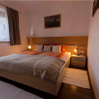 Ein einladendes Schlafzimmer mit einem großen Doppelbett, gemütlichen Kissen und warmem Licht. An der Wand hängt ein Bild, und ein Fenster lässt Tageslicht herein.