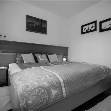 Ein gemütliches Schlafzimmer mit einem großen Bett und dekorativen Kissen. An der Wand hängen Bilder, und es gibt Nachttische mit Lampen.