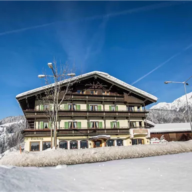 A charming wooden house in alpine style, surrounded by snow-covered mountains. The clear blue sky and the wintry landscape give the scene a festive atmosphere.