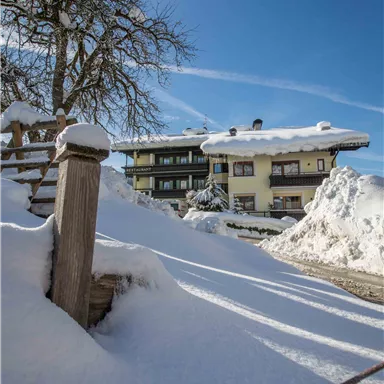 A snowy winter day with a clear sky. In the background, a cozy building can be seen, surrounded by snow.