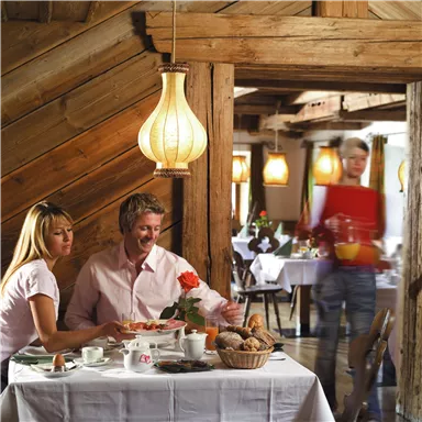 Ein gemütliches Restaurant mit rustikalem Holzinterieur. Ein Paar genießt ein Frühstück, während ein Kellner Getränke serviert.