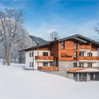 A beautiful building in the snow with a traditional wood design. The surroundings are surrounded by wintry mountains and trees.