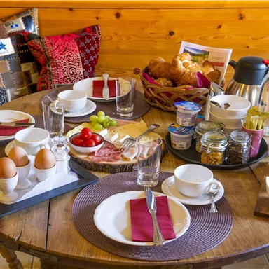 Ein schön gedeckter Frühstückstisch mit frischen Brötchen, Eiern, Obst und Getränken. Die Atmosphäre ist gemütlich und einladend.