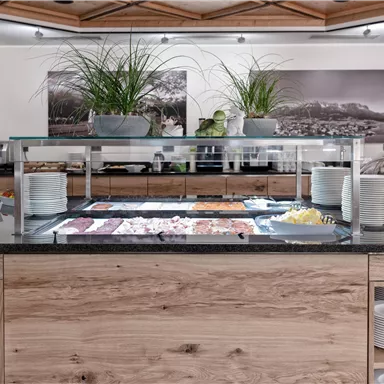 An elegant buffet area with wooden decor and fresh ingredients. The counter is tastefully decorated with various dishes and plants.