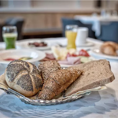 A breakfast table with various rolls and bread. In the background, drinks and other breakfast dishes can be seen.