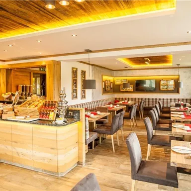 Ein modernes Restaurant mit Holzdekor und gemütlicher Atmosphäre. Tische sind mit roten Tischdecken eingedeckt und ein Frühstücksbuffet ist sichtbar.
