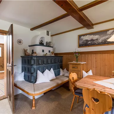 Ein gemütlicher Essbereich mit einem Holztisch und einer rustikalen Sitzecke. An der Wand befindet sich ein schöner Ofen und dekorative Elemente.