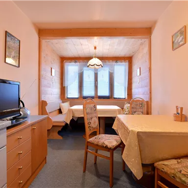 Ein gemütlicher Essbereich mit einem Tisch und mehreren Stühlen. Die Wände sind freundlich decoriert und es gibt Fenster mit Blick nach draußen.