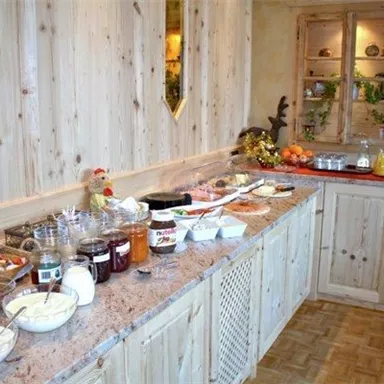 Ein einladendes Frühstücksbuffet mit verschiedenen Müsli, Marmeladen und frischen Früchten. Die Holzoberfläche und den warmen Farben verleihen eine gemütliche Atmosphäre.