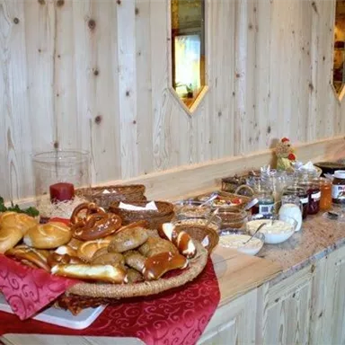 Ein reichhaltiges Frühstücksbuffet mit frischen Brötchen, Brezeln und verschiedenen Marmeladen. Der Tisch ist ansprechend dekoriert und lädt zum Genießen ein.